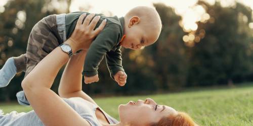maman allongée dans l'herbe soulevant son bébé