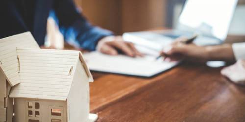 marchand de biens et conseiller en financement professionnel examinant un dossier, maquette de maison en avant plan