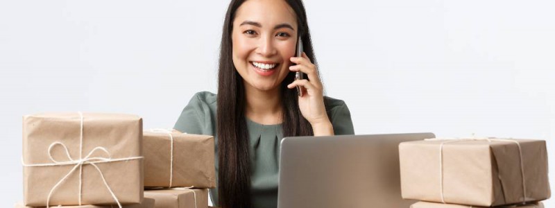Femme entrepreneure souriante devant son ordinateur au milieu colis pour ses clients