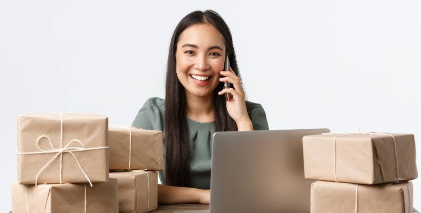 Femme entrepreneure souriante devant son ordinateur au milieu colis pour ses clients