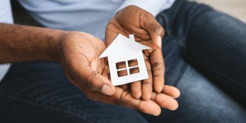 homme tenant une petite maison en carton entre ses mains