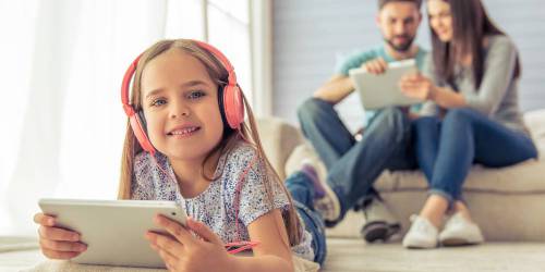 Couple de parents et leur fille souriant regardant leurs tablettes respectives.