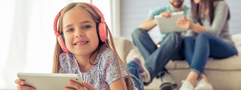 Couple de parents et leur fille souriant regardant leurs tablettes respectives.