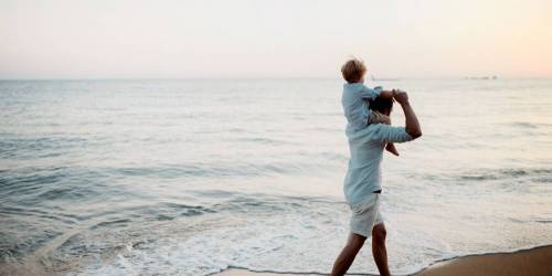 père avec son petit garçon sur les épaules marchant au bord de la mer