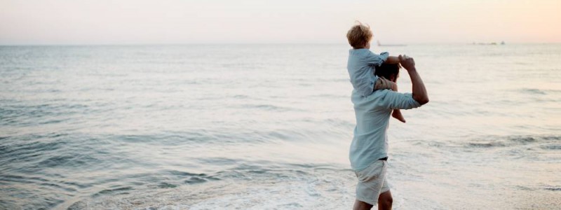 père avec son petit garçon sur les épaules marchant au bord de la mer