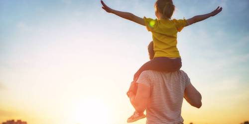 Père avec enfant sur ses épaules face au soleil couchant