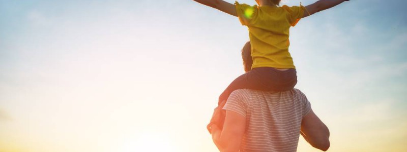 Père avec enfant sur ses épaules face au soleil couchant