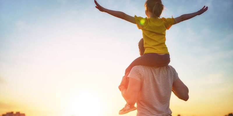 Père avec enfant sur ses épaules face au soleil couchant
