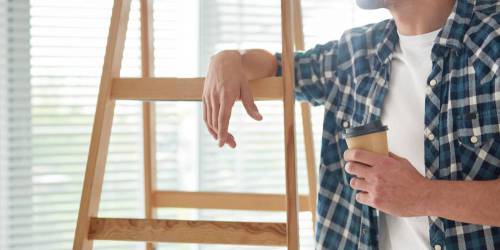 homme accouché à échelle en bois prenant une pause café durant ses travaux