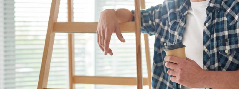 homme accouché à échelle en bois prenant une pause café durant ses travaux