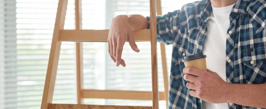 homme accouché à échelle en bois prenant une pause café durant ses travaux
